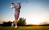 Male golf player teeing off golf ball from tee box to beautiful sunset