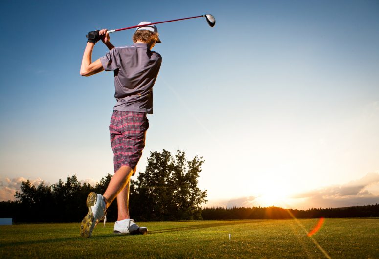 Männlicher Golfspieler, der Golfball vom Teekasten zum schönen Sonnenuntergang abschlägt